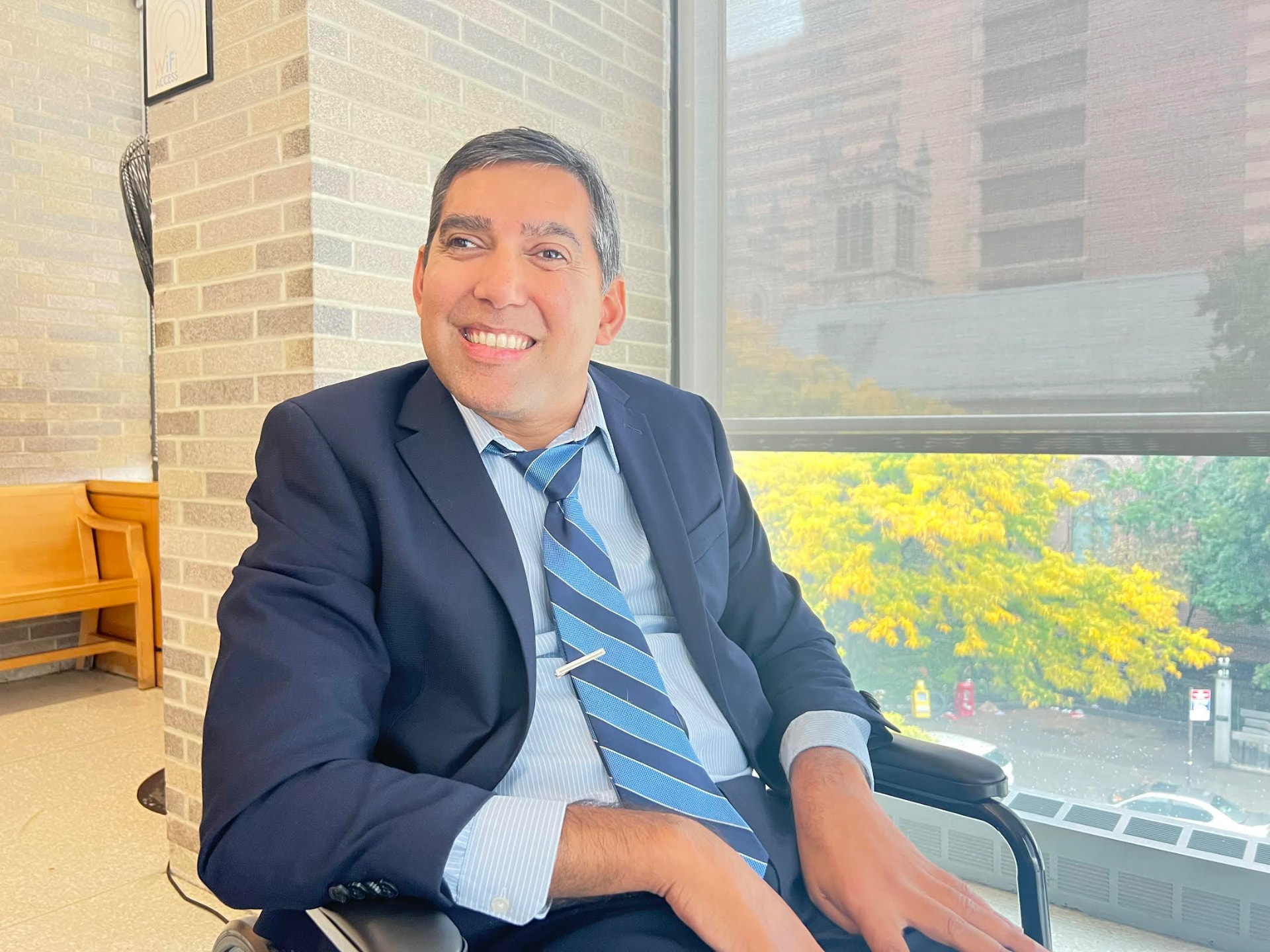 Filmmaker Jason DaSilva smiling in a navy suit beside a sunlit window